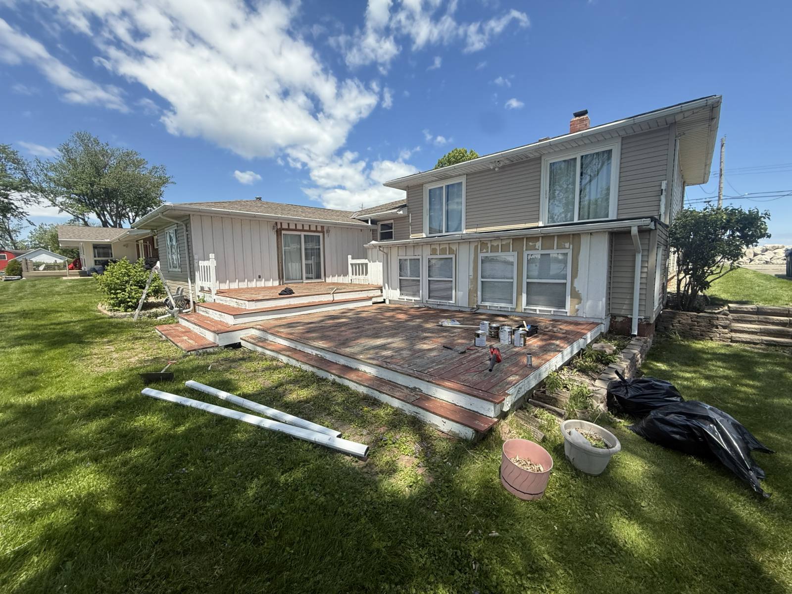 A backyard deck with peeling paint on the boards, paint cans and tools staged before refinishing