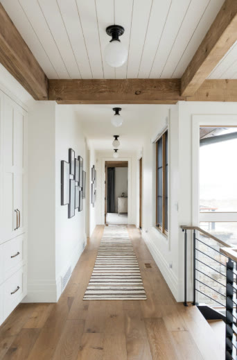 A hallway with wood flooring running in the direction of travel, a striped runner rug, and shiplap ceiling in the same alignment