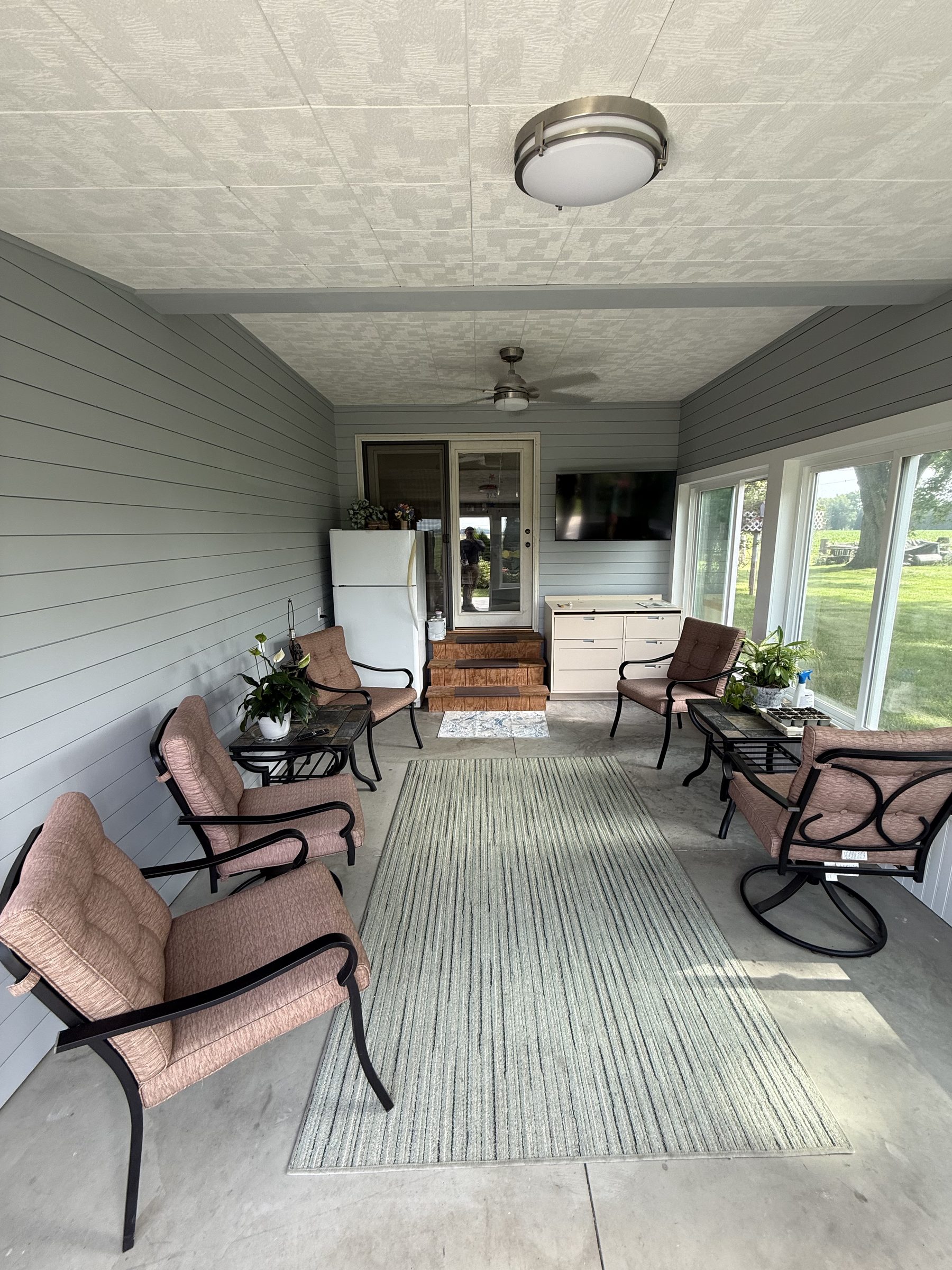 Finished sunroom remodel by Legacy Contracting Company with shiplap walls, a wall of windows, and staged furniture