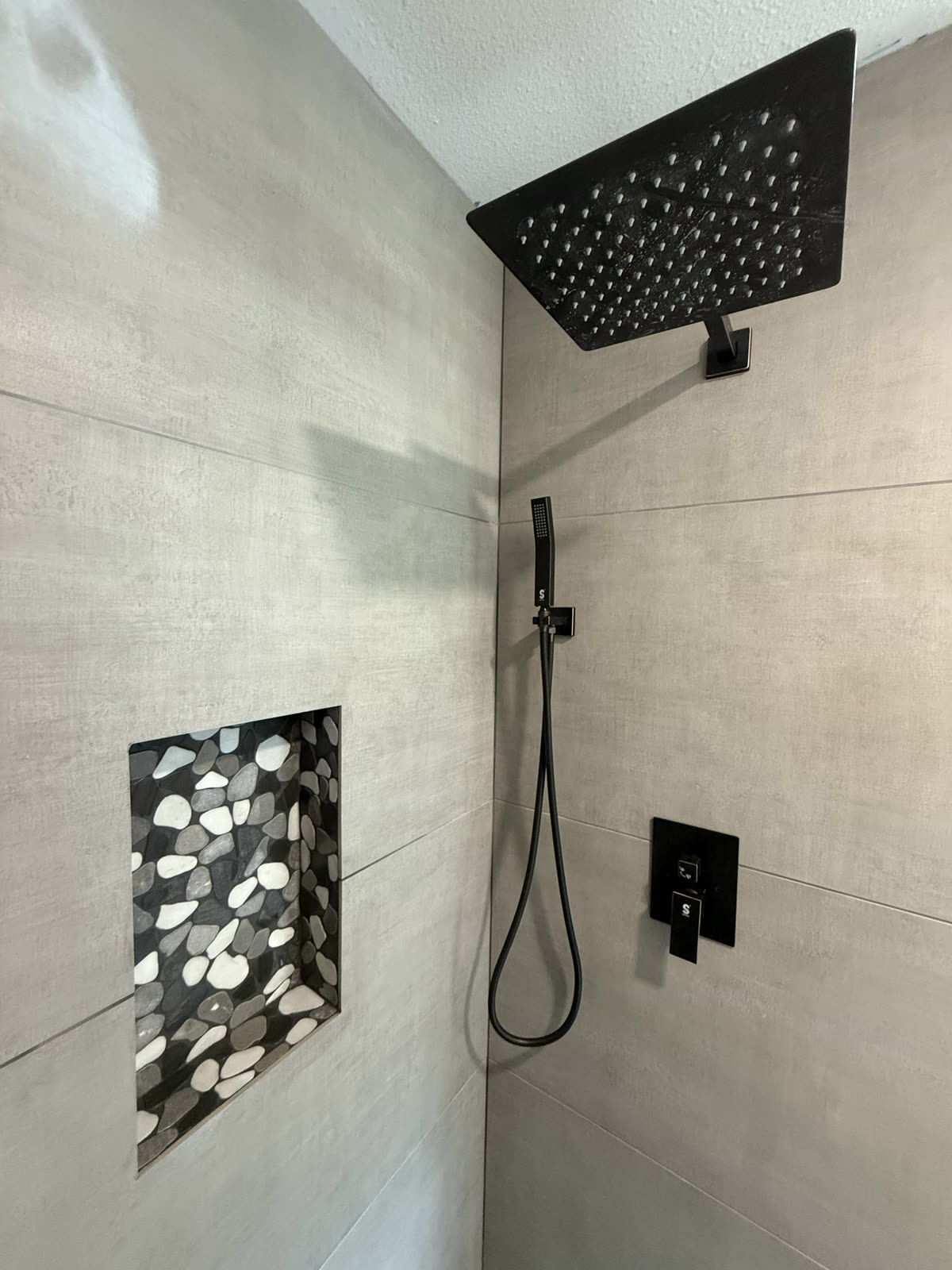 The finished mosaic niche with matte black rainhead, handheld and valve trim.